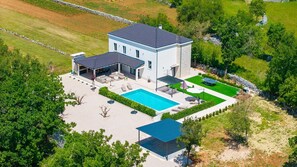 A two-story house with a swimming pool, outdoor seating, and a stone wall.