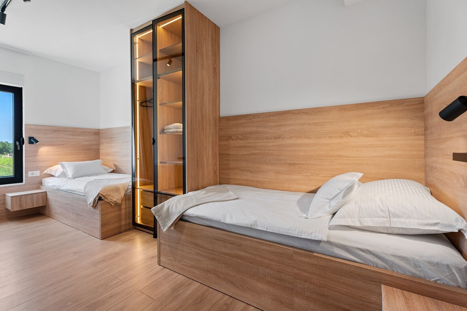 Un dormitorio moderno con cabecera de madera, armario empotrado con puertas de vidrio y ventana con vistas al exterior.