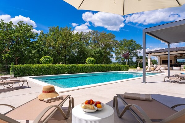 A swimming pool with lounge chairs and a covered seating area.
