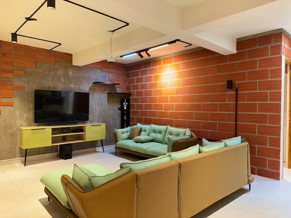 A modern living room with a brick wall, a flat-screen TV, a yellow cabinet, and a light green sofa.