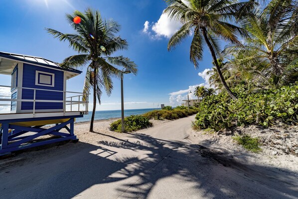 A beachside view with a lifeguard tower, palm trees, and a clear sky. - Palm By The Sea (Hollywood)