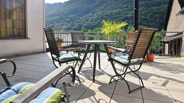 Une terrasse avec une table et des chaises, un banc et une vue sur une colline boisée.
