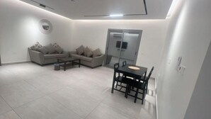 Un salon moderne avec deux canapés, une table basse et une table à manger avec des chaises. Une porte-fenêtre coulissante donne accès à un balcon.
