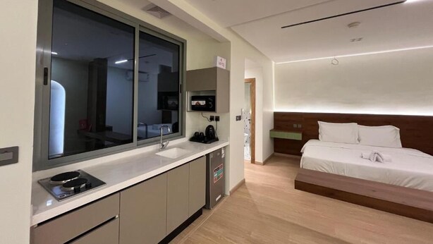 Une chambre d’hôtel moderne équipée d’une kitchenette, d’un grand miroir, d’un lit et d’une tête de lit en bois.
