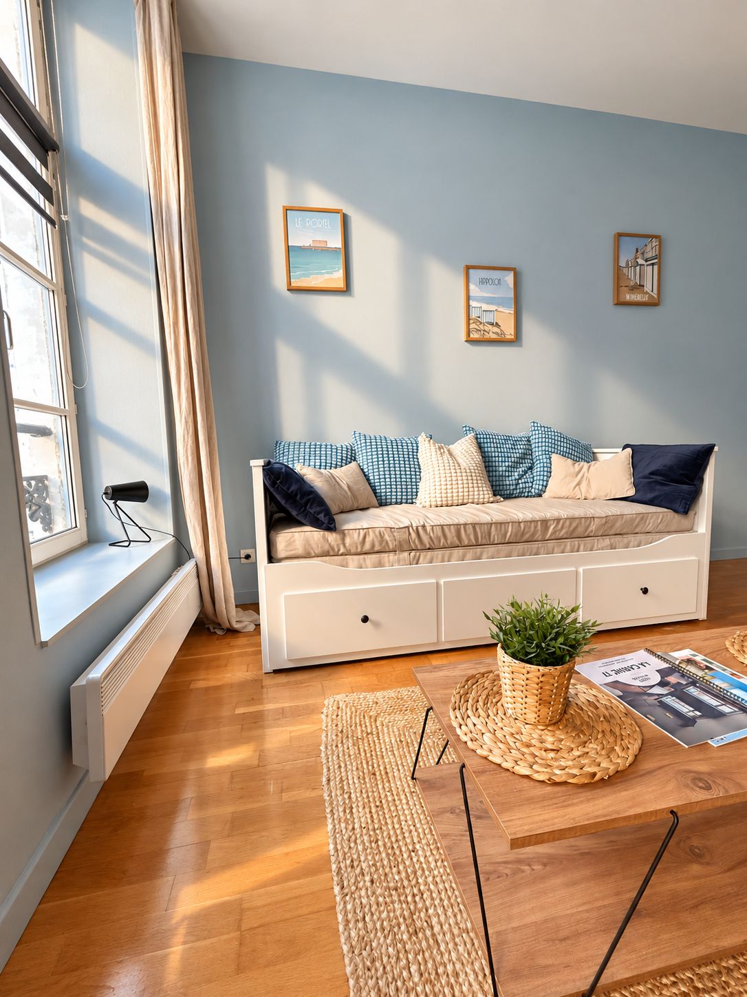 A modern living room with a sofa, a window with curtains, a radiator, a woven rug, and a small plant on a wooden table.
