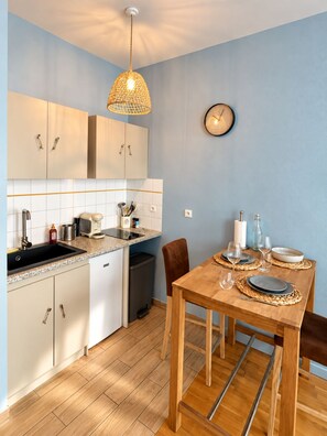 A modern kitchen with white cabinets, a granite countertop, and a wooden dining table set for two. - La Cabine 17 - Studio de Standing en Centre-Ville (Boulogne-sur-Mer)
