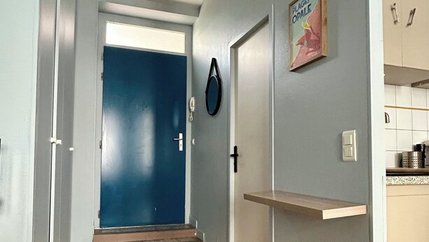 A hallway with a blue door, a woven rug, and a kitchen area with cabinets.