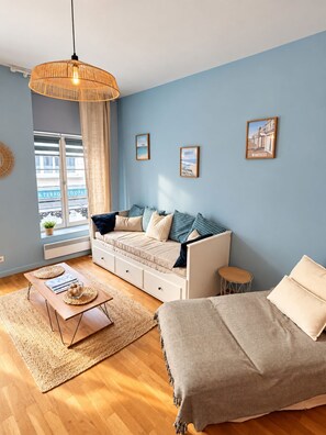 A modern living room with a sofa set, a coffee table, a hanging light fixture, and a view of the outside. - La Cabine 17 - Studio de Standing en Centre-Ville (Boulogne-sur-Mer)