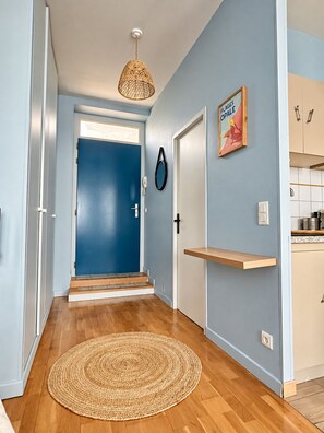 A hallway with a blue door, a woven rug, and a kitchen area with cabinets. - La Cabine 17 - Studio de Standing en Centre-Ville (Boulogne-sur-Mer)