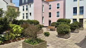 A courtyard with a wooden bench, planters, and a building with multiple windows and balconies.
