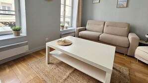 A modern living room with a beige sofa, a white coffee table, and a large window with curtains.