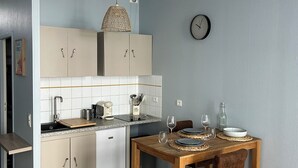 A compact kitchen with white cabinets, a wooden dining table, and a hanging light fixture.