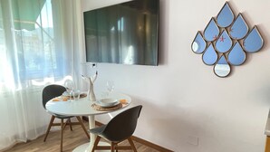 A dining area with a round table, two chairs, a flat-screen TV mounted on the wall, and a decorative wall piece. - Ferraretto cosy studio for 2 in Rapallo (Rapallo)