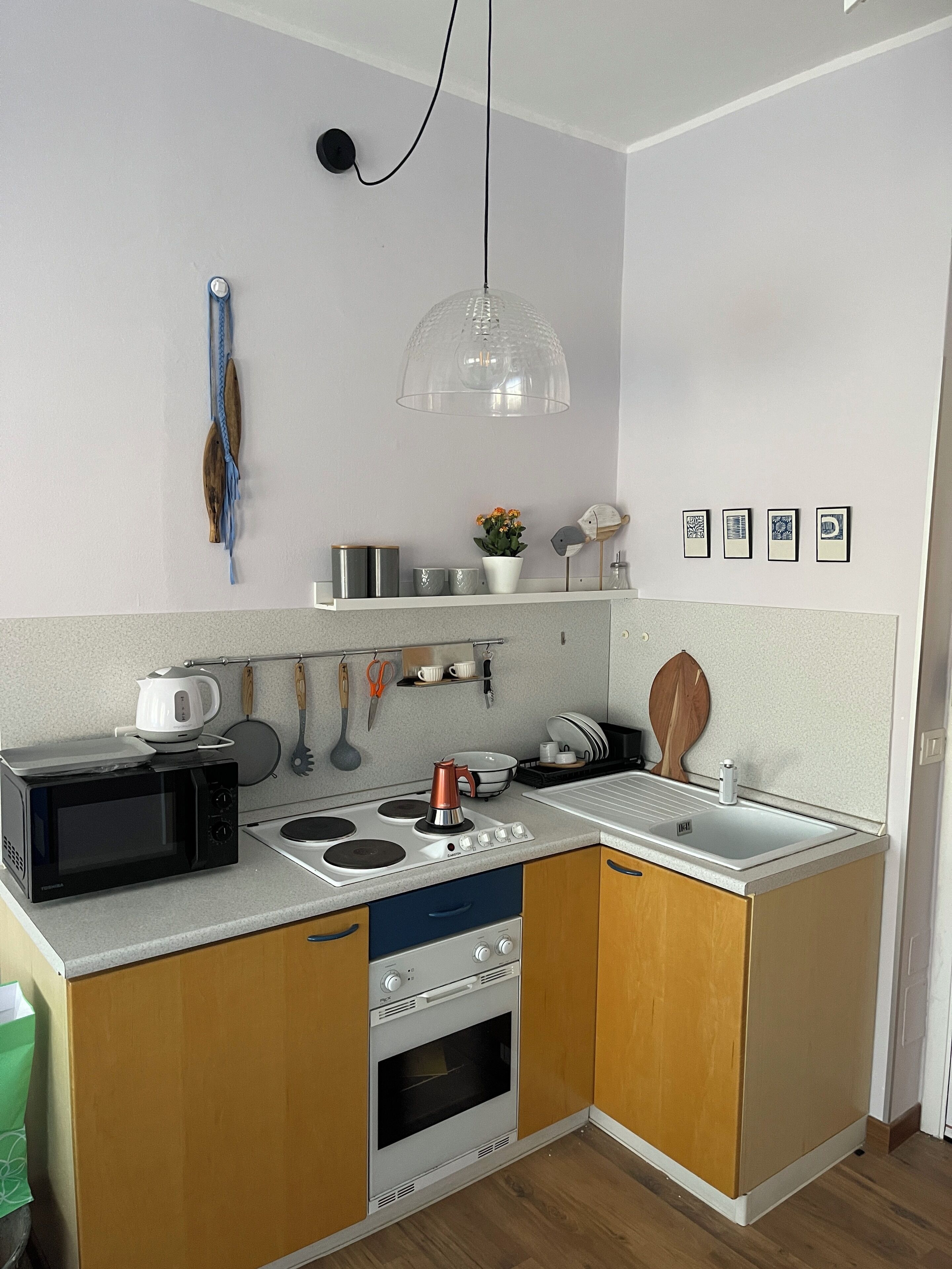 Ett kompakt kök med mikrovågsugn, spis, ugn och en hängande taklampa.
