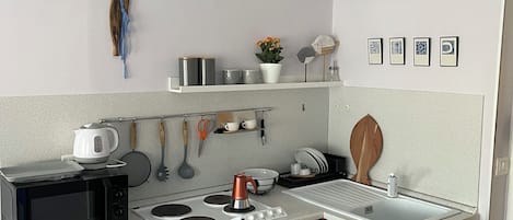 A compact kitchen with a microwave, stove, oven, and a hanging pendant light.
