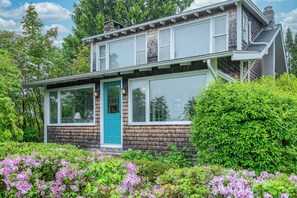 A two-story house with a prominent front door, large windows, and a well-maintained garden with flowering plants. - Charming 3BR, 2.5BA Pet-friendly home, Ocean access just a short walk away (Harpswell)