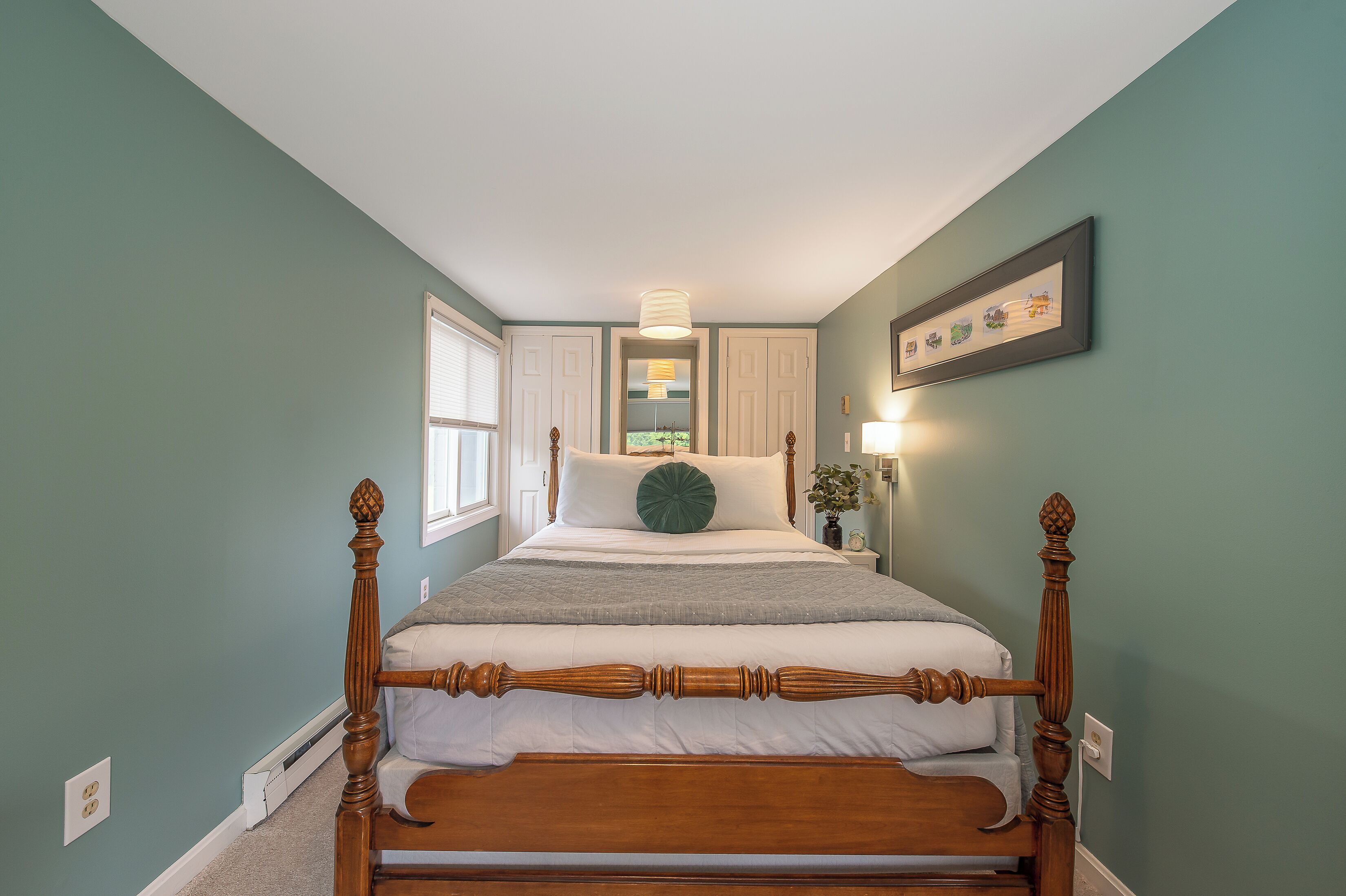 A four-poster bed with a wooden frame, a white mattress, and a green accent pillow.