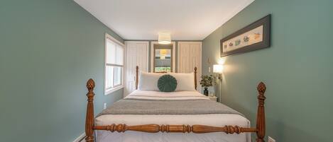 A four-poster bed with a wooden frame, a white mattress, and a green accent pillow.