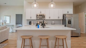 Cocina moderna con armarios blancos, refrigerador de acero inoxidable, horno doble e isla central con taburetes.