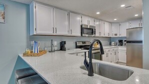 A modern kitchen with white cabinets, stainless steel appliances, a granite countertop, and a built-in oven. - Oceanfront Two Bedroom, Two Bath Horizon East Condo (Garden City Beach)