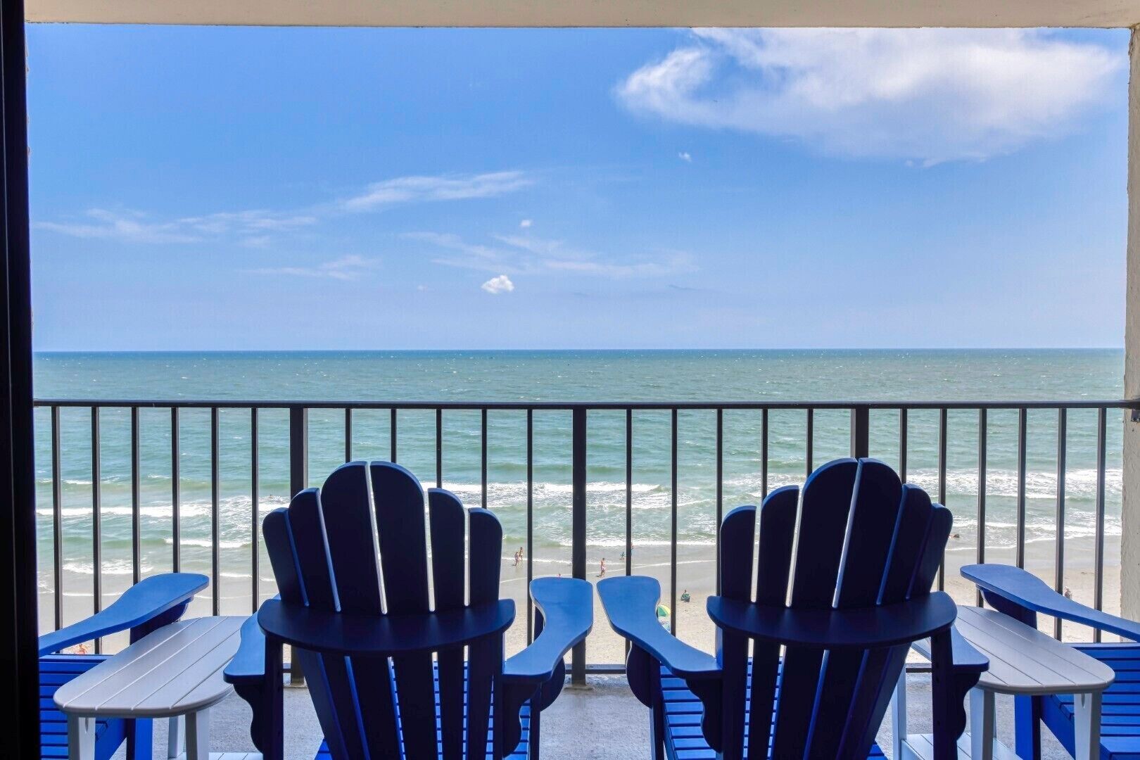 A balcony with chairs and tables overlooking a beach.