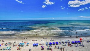 A beach with clear blue water, people swimming, and umbrellas on the sand. - Oceanfront Two Bedroom, Two Bath Horizon East Condo (Garden City Beach)