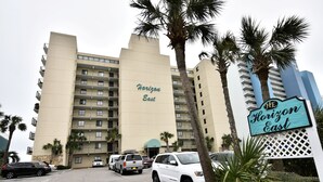A multi-story hotel named 'Horizon East' with a beige facade, multiple balconies, and a parking area with several vehicles. - Oceanfront Two Bedroom, Two Bath Horizon East Condo (Garden City Beach)