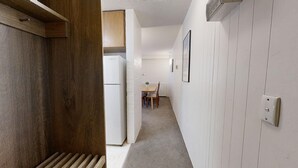 Un passadís estret amb una porta de fusta a l'esquerra, un radiador blanc, i una zona de menjador amb una taula i cadires al fons.
