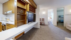 Una cuina moderna amb forn integrat, microones i un gran televisor de pantalla plana. Hi ha un armari de fusta amb prestatges i una làmpada penjant.