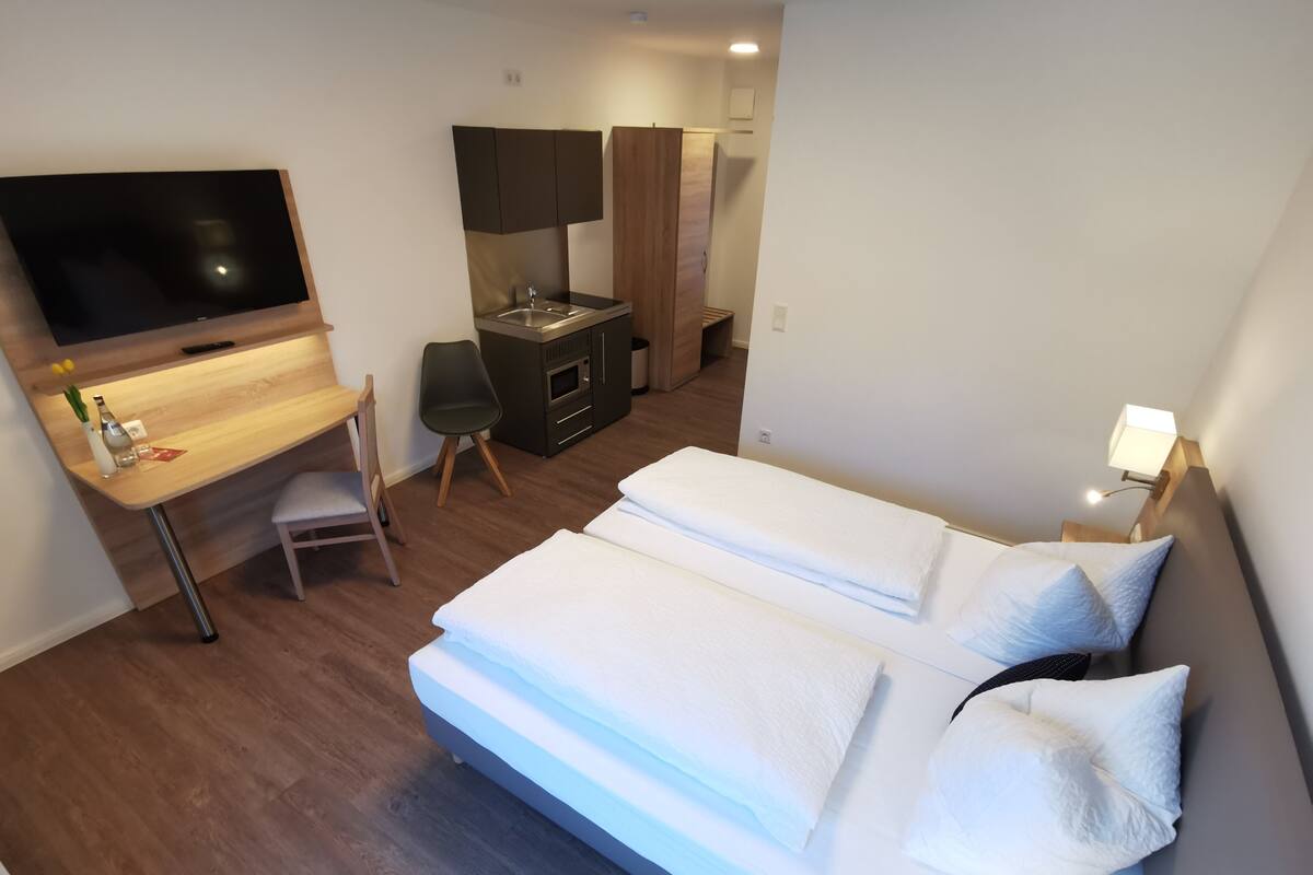 Une chambre d’hôtel équipée d’un lit, d’un bureau, d’une télévision et d’une petite kitchenette.