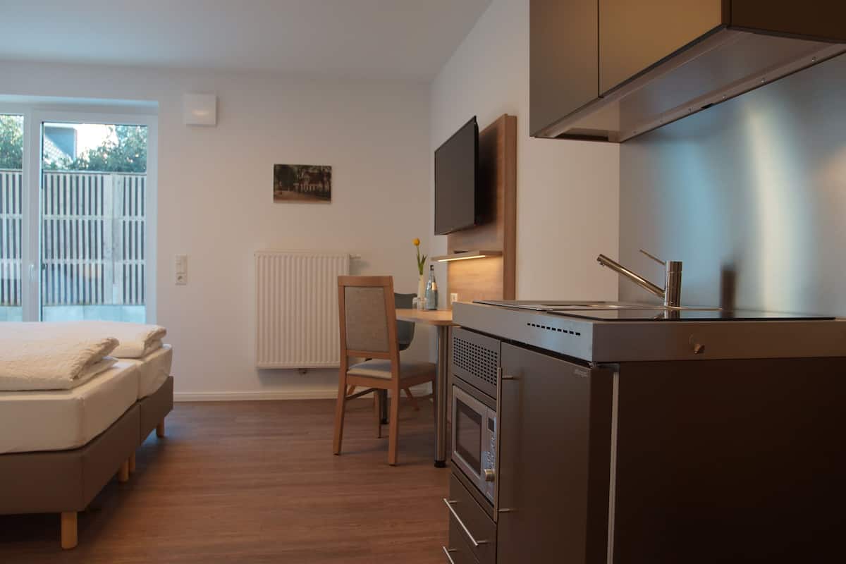 Un espace de vie compact comprenant un coin cuisine, un lit, une chaise et un téléviseur fixé au mur.