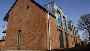 Un bâtiment en briques rouges, doté de grandes fenêtres et d’une extension en métal.