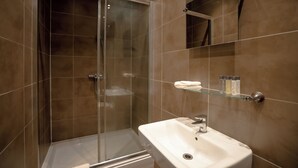 A modern bathroom with a glass-enclosed shower, a white sink, and a glass shelf with toiletries. - The Mayflower at Austerfield (Doncaster)