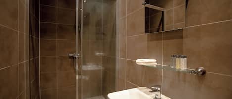 Une salle de bain moderne avec une douche à parois de verre, un lavabo blanc et une étagère en verre où sont rangés les articles de toilette.