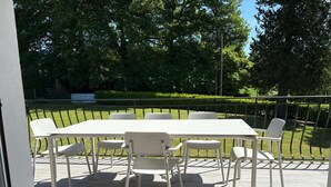 A terrace with a table and chairs, surrounded by a metal railing, overlooking a well-maintained garden. - Family home (Eymoutiers)
