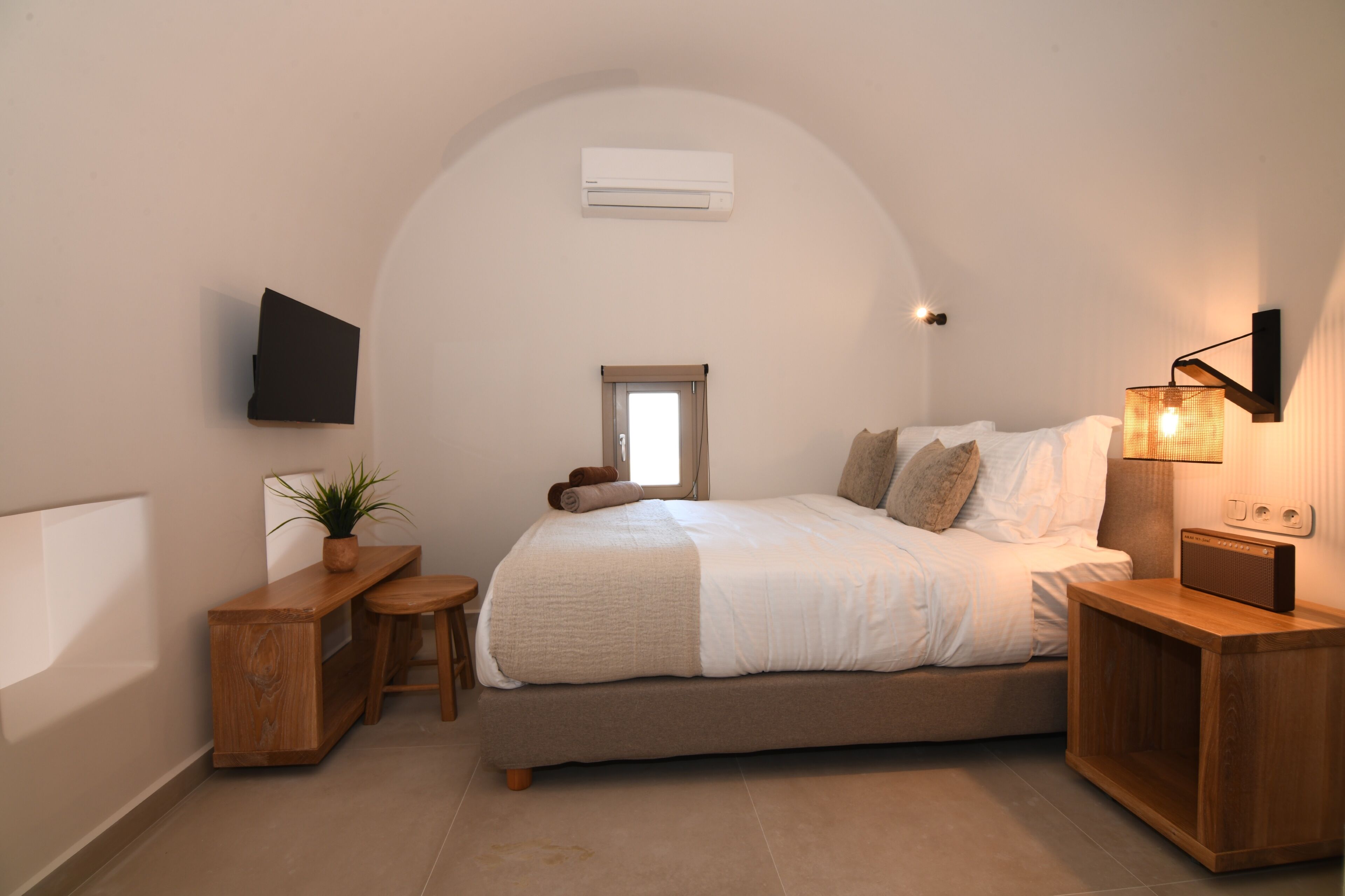 Ein Schlafzimmer mit Bett, Nachttisch, Lampe, Fernseher und einem kleinen Fenster.