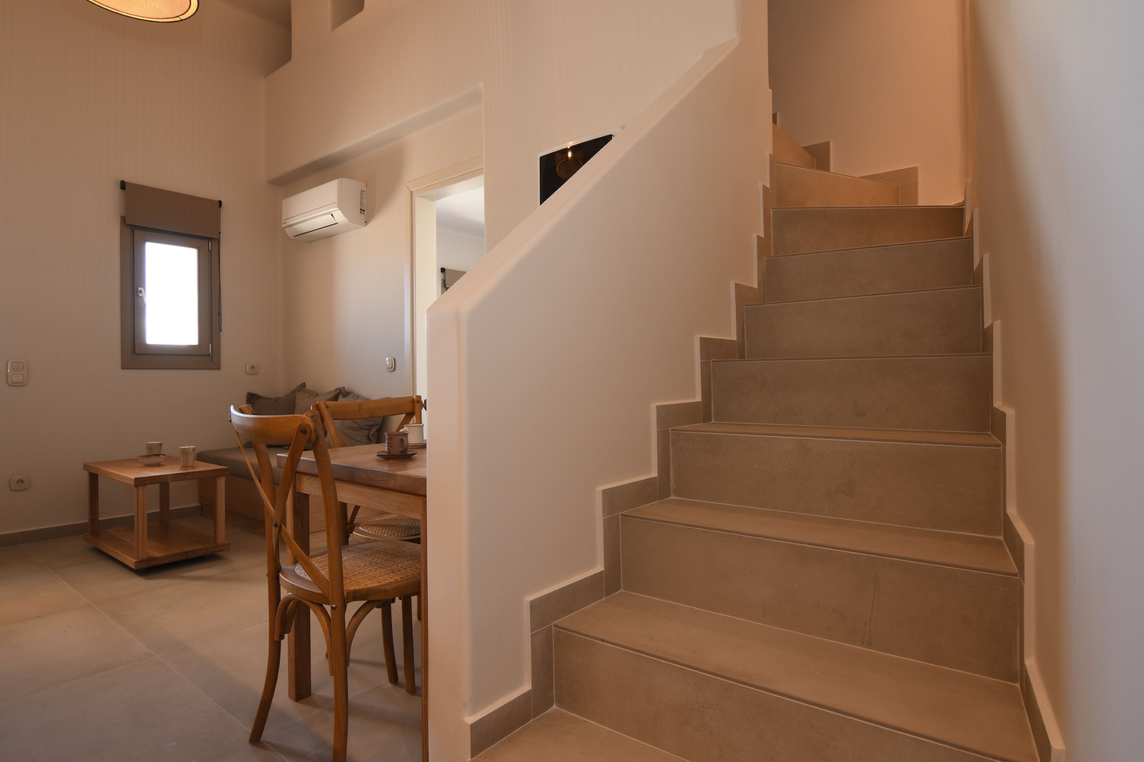 A staircase leading to an upper floor, a dining area with a table and chairs, and a small window with blinds.
