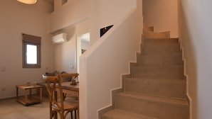 Una escalera que sube a un piso superior, un comedor con mesa y sillas, y un ventanal con persianas.