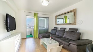 A modern living room with a brown leather sofa, a glass coffee table, and a flat-screen TV mounted on the wall.