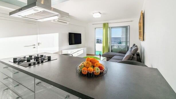A modern kitchen with a central island, a flat-screen TV, and a dining area with a sofa.
