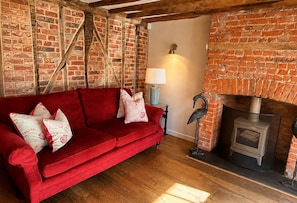 A red sofa with floral cushions in a room with exposed brick walls and a fireplace.