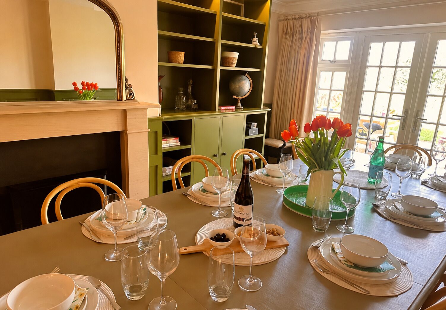 A dining table set for a meal with plates, glasses, and a bottle of wine.