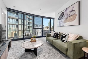 A modern living room with a green sofa, a round coffee table, and a large window offering a city view. - CBD Luxe Pad SkyTower Pool & Gym Brisbane City (Brisbane City)