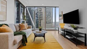 A modern living room with a sofa, coffee table, and TV. - Platinum Pad Westside Place, Balcony, Heated Pool, Gym, Sauna, Steam. (Melbourne)