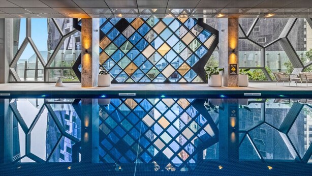 A modern indoor pool with geometric glass panels and a clear view of the cityscape. - Platinum Pad Westside Place, Balcony, Heated Pool, Gym, Sauna, Steam. (Melbourne)