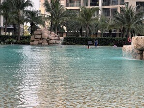 Una piscina con agua cristalina, rodeada de palmeras y una formación rocosa.