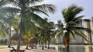 A beach with palm trees, a thatched-roof pavilion, and a calm water body. - Vinhomes Grand Park-The Beverly Hills (Ho Chi Minh City)