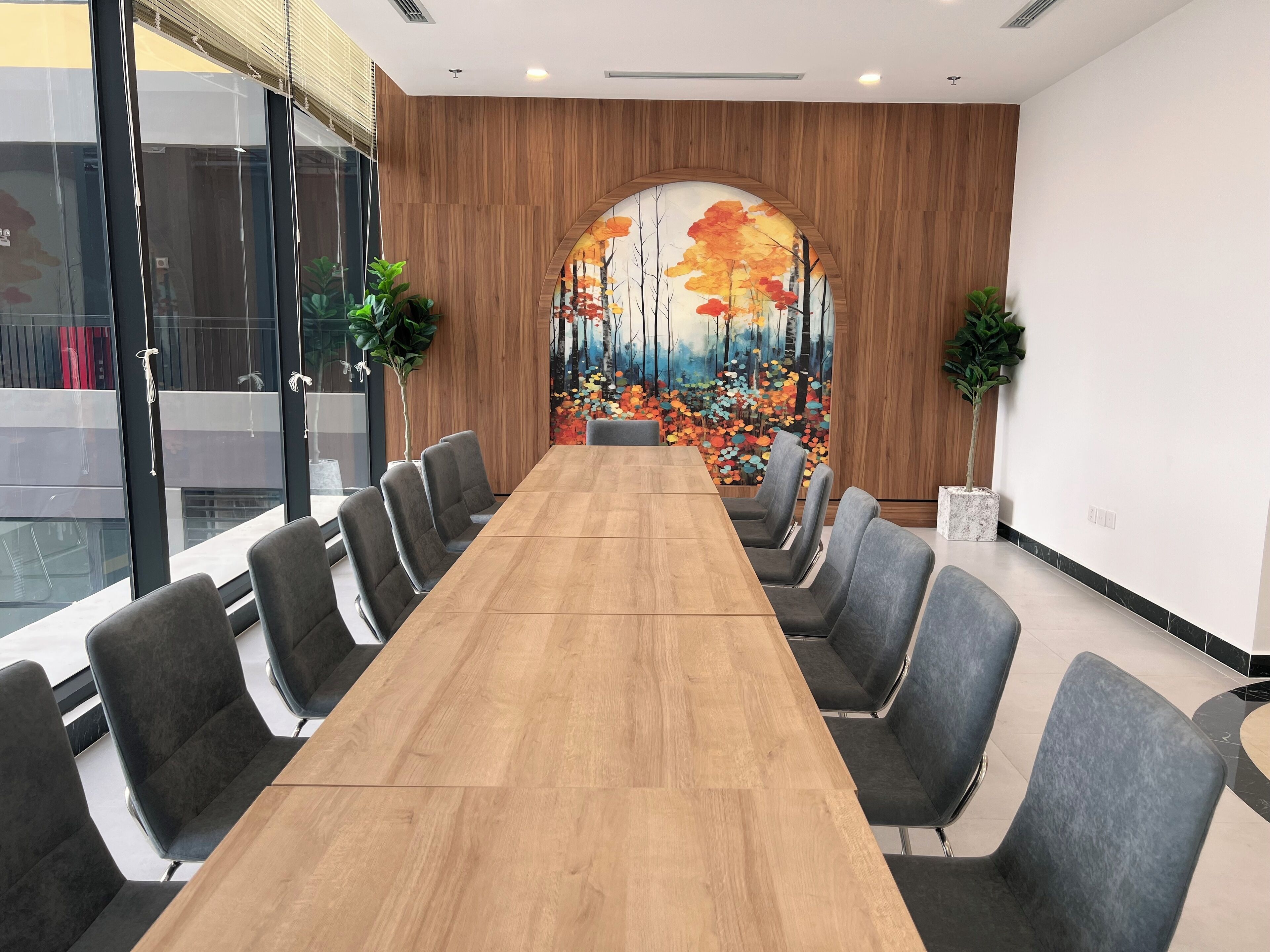 A conference room with a long wooden table and grey upholstered chairs.