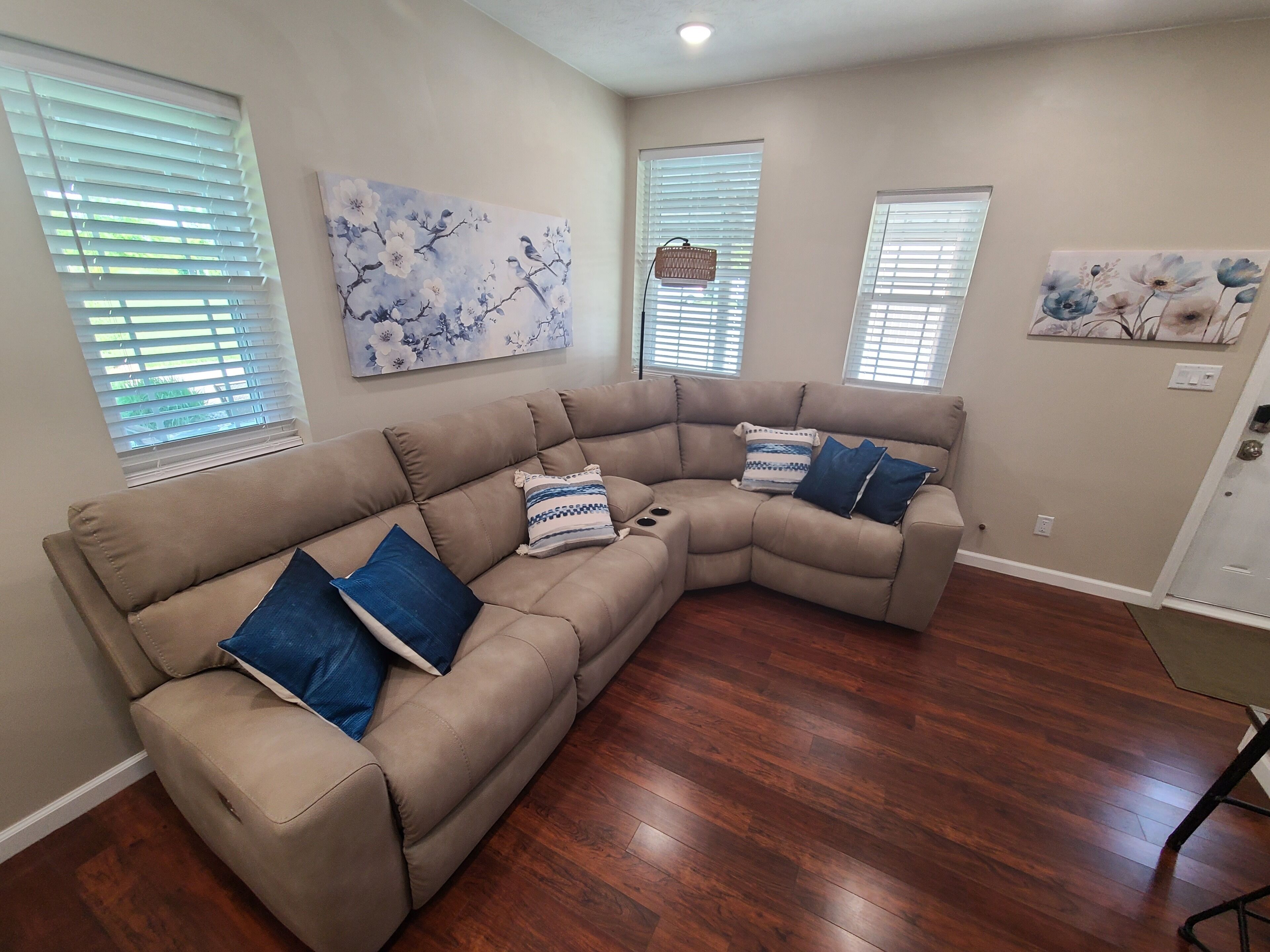 A living room with a beige sectional sofa, two side tables, and a wooden floor.