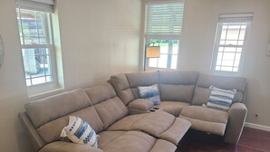 Un sofá modular con función reclinable, ubicado en una habitación con piso de madera y paredes blancas.